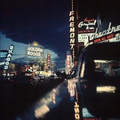 a car driving down a street next to tall buildings with neon signs on the side of it