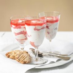 three glasses filled with dessert sitting on top of a white plate next to a cookie