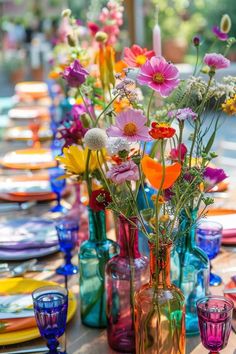 colorful glass vases filled with flowers sit on a table set for an outdoor dinner