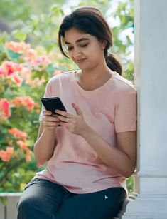 a woman sitting on a ledge looking at her cell phone while she's texting