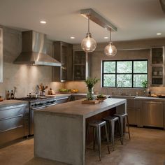 a large kitchen with stainless steel appliances and counter tops, along with two stools