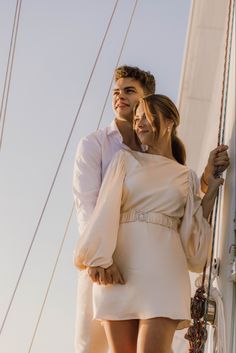 a man and woman standing next to each other on a sailboat in the ocean