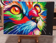 a colorful cat painting on an easel in front of some other art work items