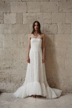 a woman standing in front of a brick wall wearing a white dress with flowers on it