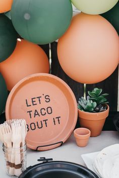 a table topped with balloons and plates next to potted plants on top of a table