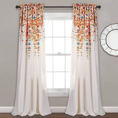 a white curtain with colorful flowers on it in front of a mirror and wall hanging