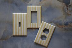 three yellow and white striped switch plates on a marble surface with holes in the middle