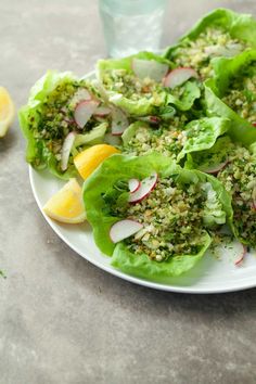 some lettuce and radishes are on a plate with lemon wedges