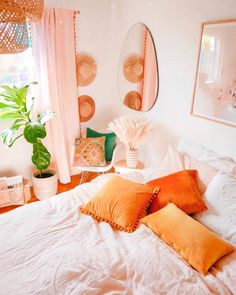 a white bed topped with lots of pillows next to a potted plant and window