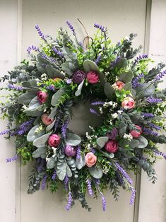 a wreath is hanging on the door with purple flowers and greenery around it,