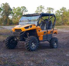 an orange four - wheeled vehicle parked in the middle of a dirt field with trees behind it