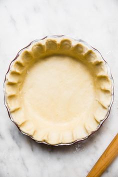 an uncooked pie crust sits on a marble countertop next to a wooden utensil