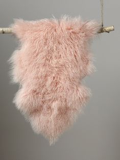 a pink furry animal ornament hanging from a twig on a gray background