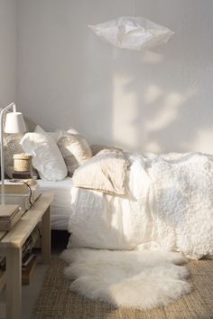 a white bed sitting in a bedroom next to a wooden table and lamp on top of a hard wood floor