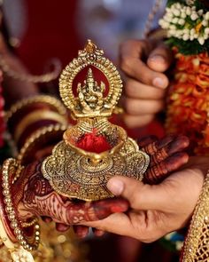 two hands are holding a gold and red object in front of other people's hands