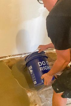 a man in black shirt painting walls with blue paint on the wall and another person holding a bucket