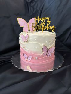 a pink and white cake with butterflies on it's top is sitting on a black surface