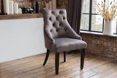 a grey chair sitting in front of a window next to a brick wall and wooden floor