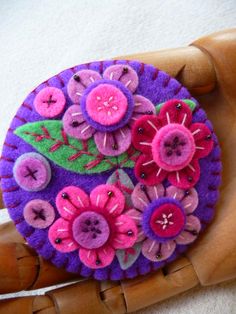 a close up of a person's hand holding a purple and pink flower brooch