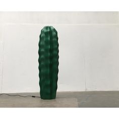 a large green vase sitting on top of a cement floor next to a white wall