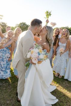 a bride and groom kissing in front of their wedding party