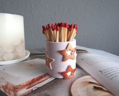 matches are placed in a cup next to an open book and candle on a table