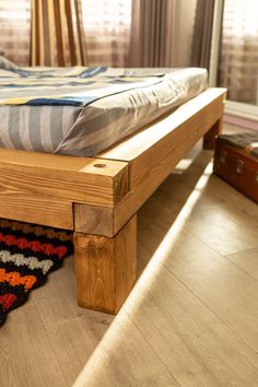 a wooden bed frame sitting on top of a hard wood floor next to a window