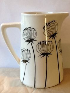 a white pitcher with black flowers painted on the front and sides, sitting on a table