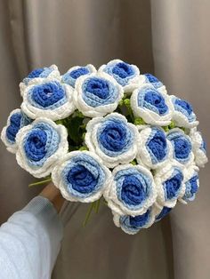 a bouquet of blue and white crocheted flowers is held by a woman's hand