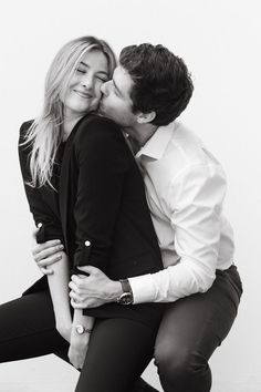 a man and woman kissing each other while sitting on top of one another in front of a white wall