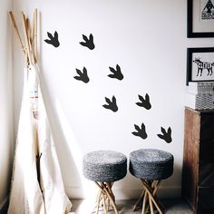 two stools in front of a white wall with black birds on it and a teepee