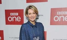 a woman standing in front of a red and white wall wearing a blue shirt with flowers on it