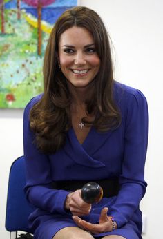 a woman sitting in a blue chair holding an object with one hand and smiling at the camera