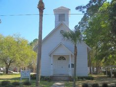 an old white church with palm trees in front