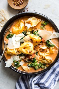 a bowl of tortellini soup with spinach, cheese and other toppings