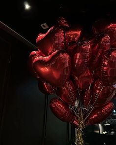 a bunch of red heart shaped balloons hanging from a ceiling in a dark room with city lights behind them