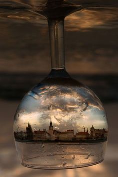 an upside down view of a city in a wine glass that is reflecting the sky and clouds