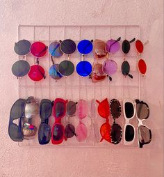 several pairs of sunglasses are displayed on a rack against a pink wall with white paint