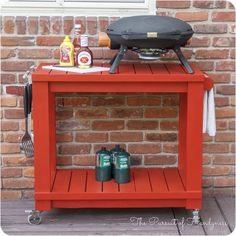 an orange cart with grill on top next to brick wall and cooking utensils