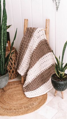 a crocheted blanket sitting on top of a rug next to potted plants