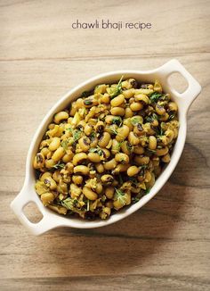 a white bowl filled with beans and greens on top of a wooden table next to a spoon