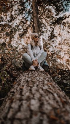 a woman sitting on top of a large tree in the middle of a wooded area