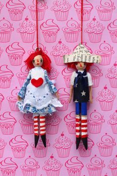 two dolls are hanging on the wall with cupcakes in the background and one is holding a sign that says i love you