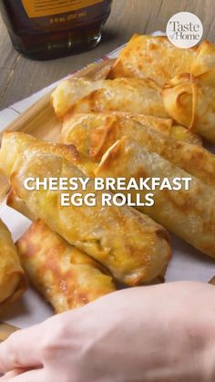 cheesey breakfast egg rolls on a cutting board next to a bottle of maple syrup