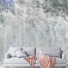 a white couch sitting in front of a forest wall mural