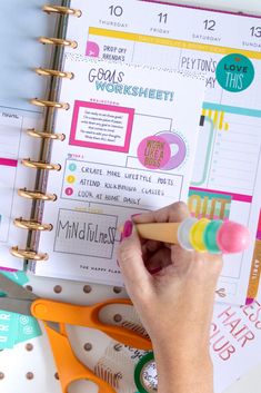 a person is writing on a planner page with scissors and other items around it,