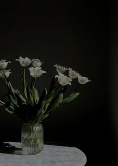 some white flowers are in a glass vase on a table with a black back ground