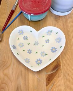 a heart shaped dish sitting on top of a wooden table next to other bowls and utensils