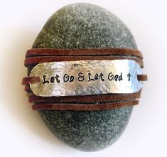 "Wear your daily affirmations and inspirational words on your wrist to remind yourself of what is most important to you every day. :) This leather wrap bracelet features the phrase \"Let Go and Let God\", hand stamped onto hammered aluminum. The soft brown faux suede leather cord is approximately 36\" long and can usually wrap around the wrist 2 times. The. Just tie a loose knot or two in the back to secure and you are good to go! You can have this bracelet with or without the tiny cross at the God Bracelet, Let Go Let God, Nail Cross Necklace, God Hand, Bible Verse Bracelet, Faith Bracelet, Christian Bracelets, Let Go And Let God, Handstamped Bracelet