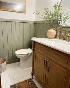 the bathroom is decorated in green and white with wood paneling on the walls, along with a gold framed mirror